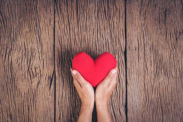Manos sosteniendo un corazón rojo de tela sobre fondo de madera rústica