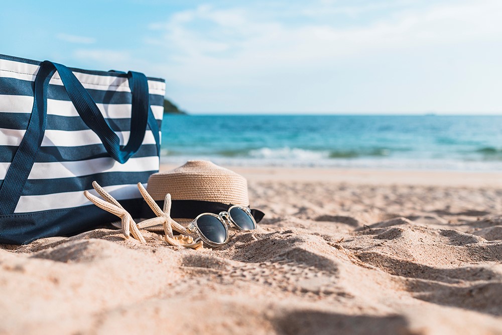 Bolsa de rayas, sombrero de paja, gafas de sol y estrella de mar sobre la arena de la playa junto al mar