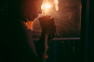 Mujer de perfil sosteniendo una taza junto a una ventana con luz cálida del atardecer