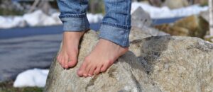 Pies descalzos con vaqueros arremangados sobre una roca junto a nieve en un entorno natural