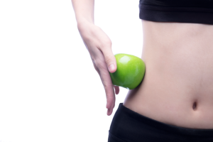 Mujer con vientre plano sujetando una manzana verde junto a su cintura