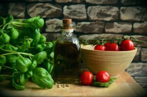 Botella de aceite de oliva con albahaca fresca y tomates cherry en cuenco sobre tabla de madera