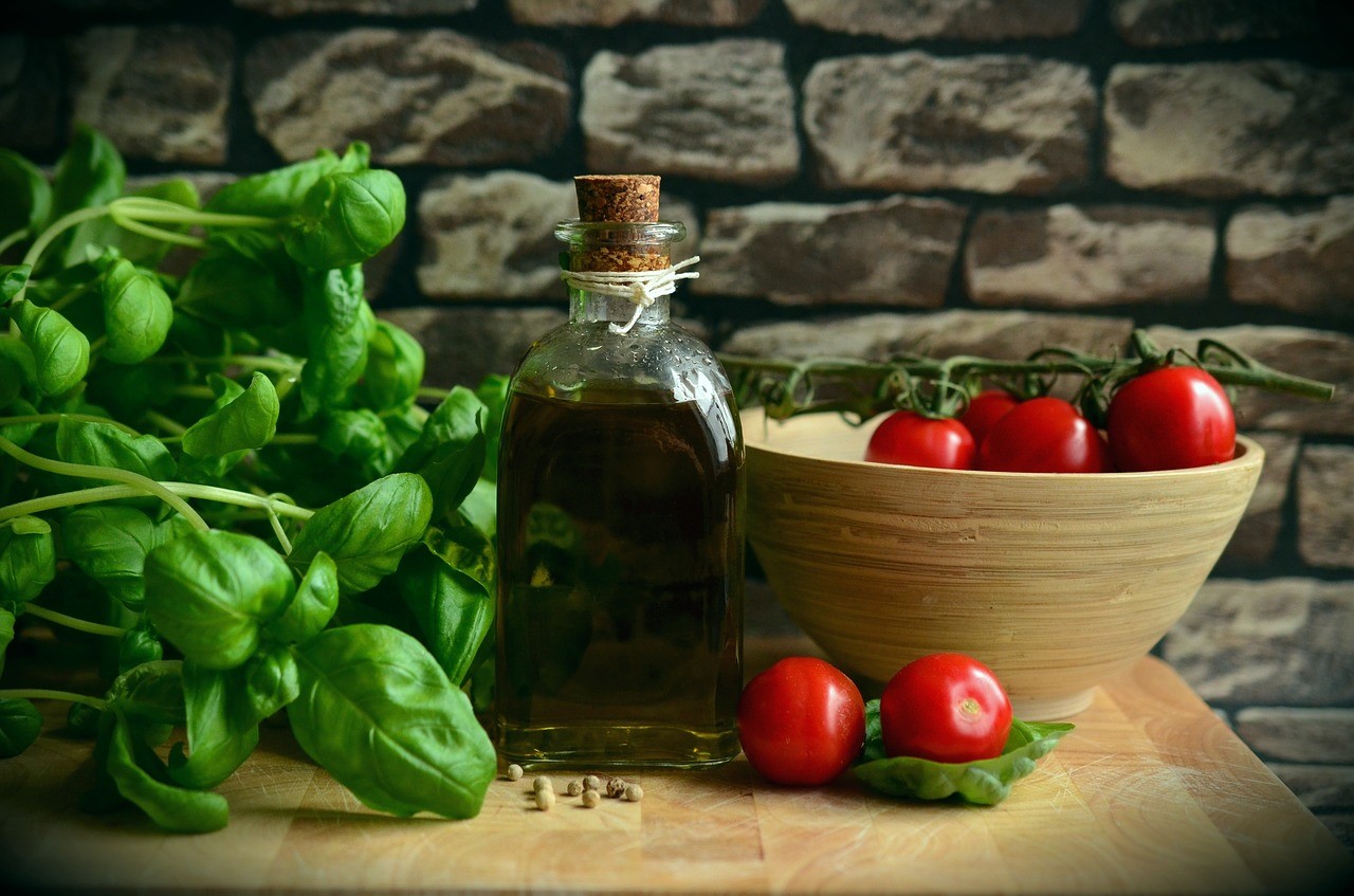 Botella de aceite de oliva con albahaca fresca y tomates cherry en cuenco sobre tabla de madera