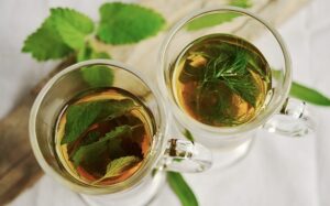 Dos tazas de cristal con infusión de hierbas, menta fresca y eneldo sobre fondo claro