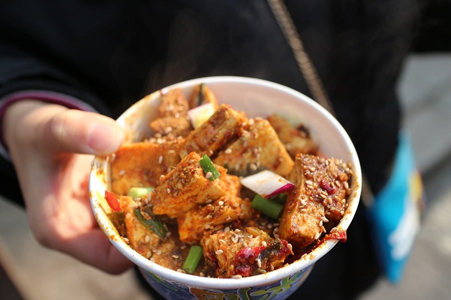 Mano sosteniendo vaso de tofu picante humeante con sésamo, chile y cebolleta como comida callejera