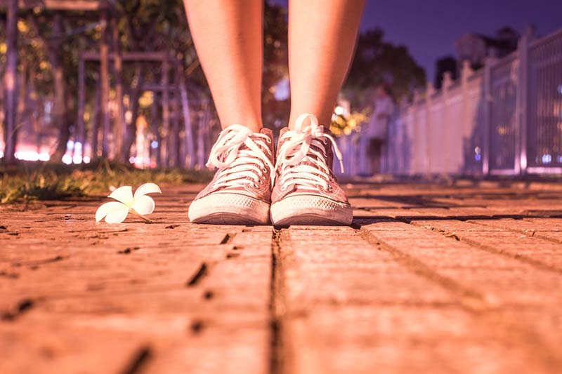 Piernas con zapatillas rosas sobre suelo empedrado junto a una flor blanca de noche