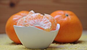 Gajos pelados de mandarina en un cuenco blanco con dos mandarinas enteras al fondo