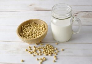 Bol de madera con granos de soja y vaso de leche vegetal sobre mesa de madera blanca