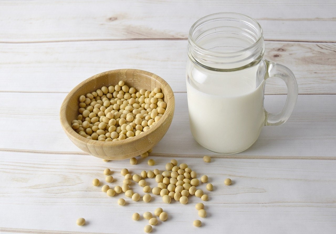 Bol de madera con granos de soja y vaso de leche vegetal sobre mesa de madera blanca