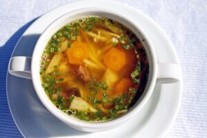 Sopa de fideos con caldo, zanahoria y cebollino en taza blanca sobre plato