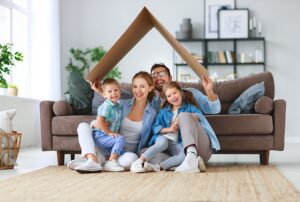 Familia sonriente con dos hijos sentada en el suelo del salón sujetando un tejado de cartón