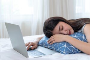 Mujer joven cansada durmiendo sobre un cojín azul junto a un portátil en la cama
