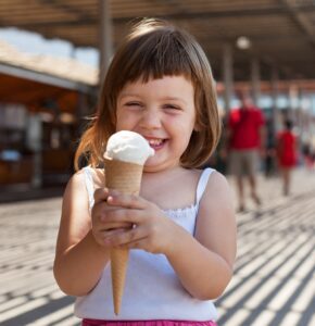 Niña sonriente sujeta un helado de cucurucho de vainilla en un paseo veraniego