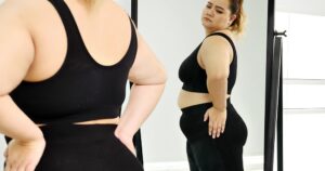 Mujer de talla grande en ropa deportiva negra mirándose de perfil en un espejo