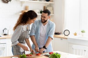 Pareja sonriente cocinando junta en la cocina, cortando verduras frescas para preparar una cena saludable