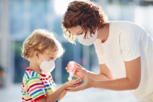 Madre con mascarilla aplica gel hidroalcohólico en las manos de un niño con camiseta de rayas