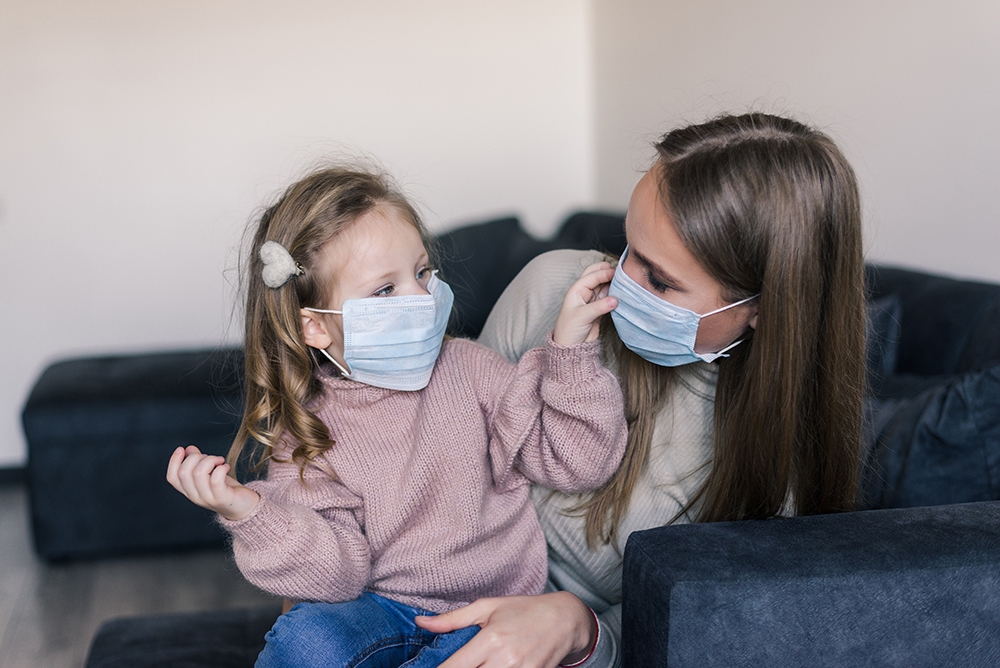 Madre e hija sentadas en un sofá con mascarillas quirúrgicas mirándose de frente