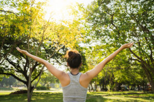 Mujer de espaldas con brazos abiertos disfrutando del sol entre árboles en un parque