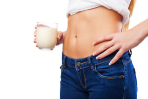 Mujer con vientre plano y vaqueros sosteniendo un vaso de leche junto a su abdomen