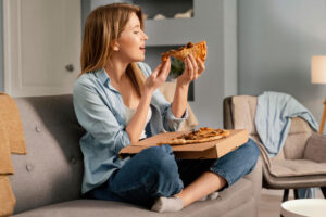 Mujer sentada en el sofá comiendo una porción de pizza sobre la caja