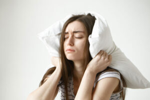 Mujer con los ojos cerrados y gesto de agotamiento tapándose los oídos con una almohada