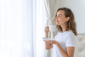 Mujer disfrutando del aroma de una taza de infusión junto a una ventana luminosa