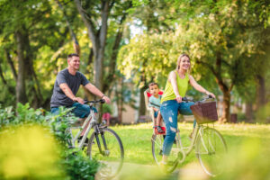Familia paseando en bicicleta por un parque con árboles verdes durante el verano