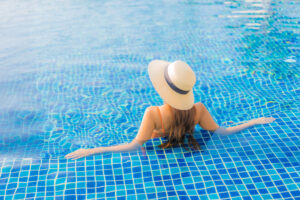 Mujer de espaldas con sombrero de paja relajándose en el borde de una piscina de agua azul