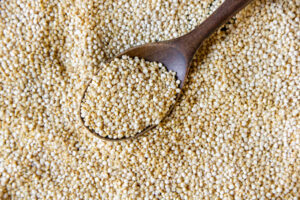 Cuchara de madera con granos de quinoa blanca sobre un fondo lleno de quinoa