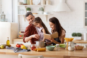 Familia cocinando junta en la cocina mientras la madre lee una receta y el padre remueve una olla