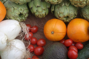Alcachofas, naranjas, cebollas, tomates cherry y aguacate frescos sobre mesa de madera
