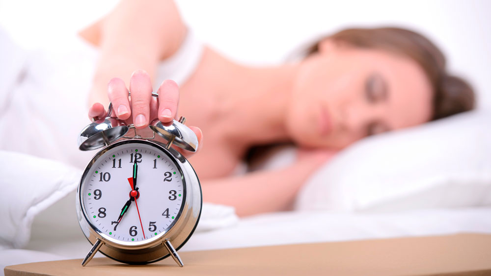 Mujer dormida en la cama apaga el despertador de metal con la mano por la mañana