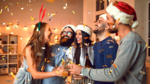 Grupo de amigos con gorros de Papá Noel brindando entre confeti dorado en una fiesta de Nochevieja