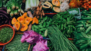 Puesto de mercado con verduras y frutas frescas como calabaza, judías verdes, pepinos, papaya y berenjenas