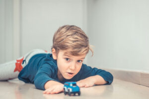 Niño rubio tumbado en el suelo jugando concentrado con un coche de juguete azul