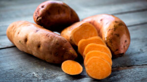 Batatas o boniatos enteros y en rodajas de pulpa naranja sobre mesa de madera rústica