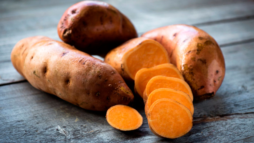 Batatas o boniatos enteros y en rodajas de pulpa naranja sobre mesa de madera rústica