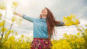 Mujer sonriente con los brazos abiertos disfrutando del sol en un campo de flores amarillas