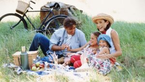 Familia con dos niñas haciendo un picnic sobre la hierba junto a una bicicleta y una cesta en primavera