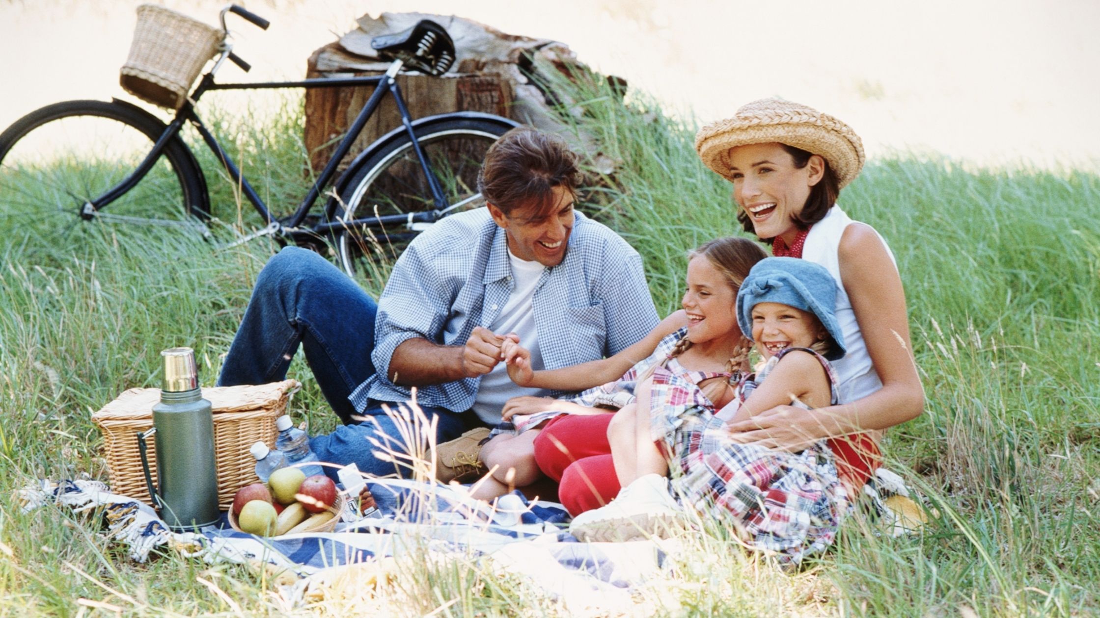 Familia con dos niñas haciendo un picnic sobre la hierba junto a una bicicleta y una cesta en primavera
