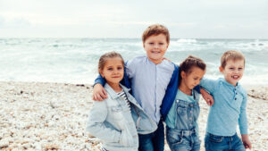 Cuatro niños sonrientes abrazados en una playa de piedras junto al mar