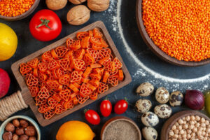 Pasta de lentejas rojas en forma de corazón sobre tabla de madera con lentejas, tomates, nueces y huevos