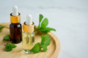 Dos frascos de aceite esencial de menta con cuentagotas y hojas frescas sobre bandeja de madera
