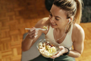 Mujer sonriente con ropa deportiva comiendo una ensalada saludable tras entrenar