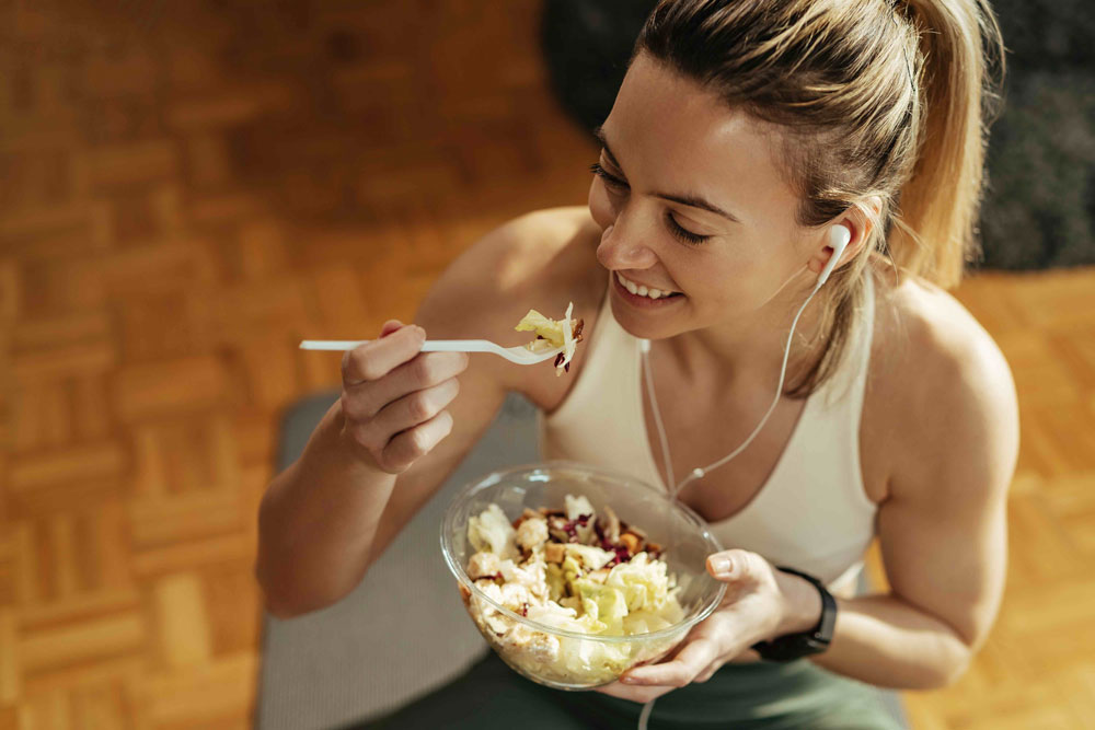 Mujer sonriente con ropa deportiva comiendo una ensalada saludable tras entrenar