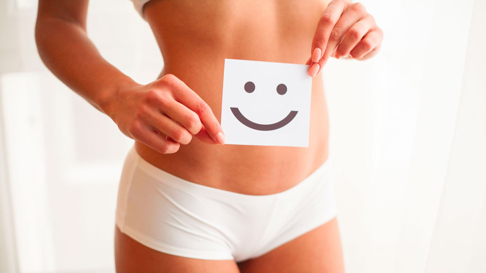Mujer en ropa interior sujeta un papel con una cara sonriente sobre su vientre saludable