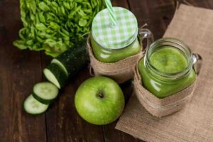 Batidos verdes detox en tarros de cristal con lechuga, pepino en rodajas y manzana verde sobre mesa de madera