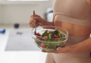 Mujer en ropa deportiva sostiene un bol de ensalada de espinacas y tomates con cuchara
