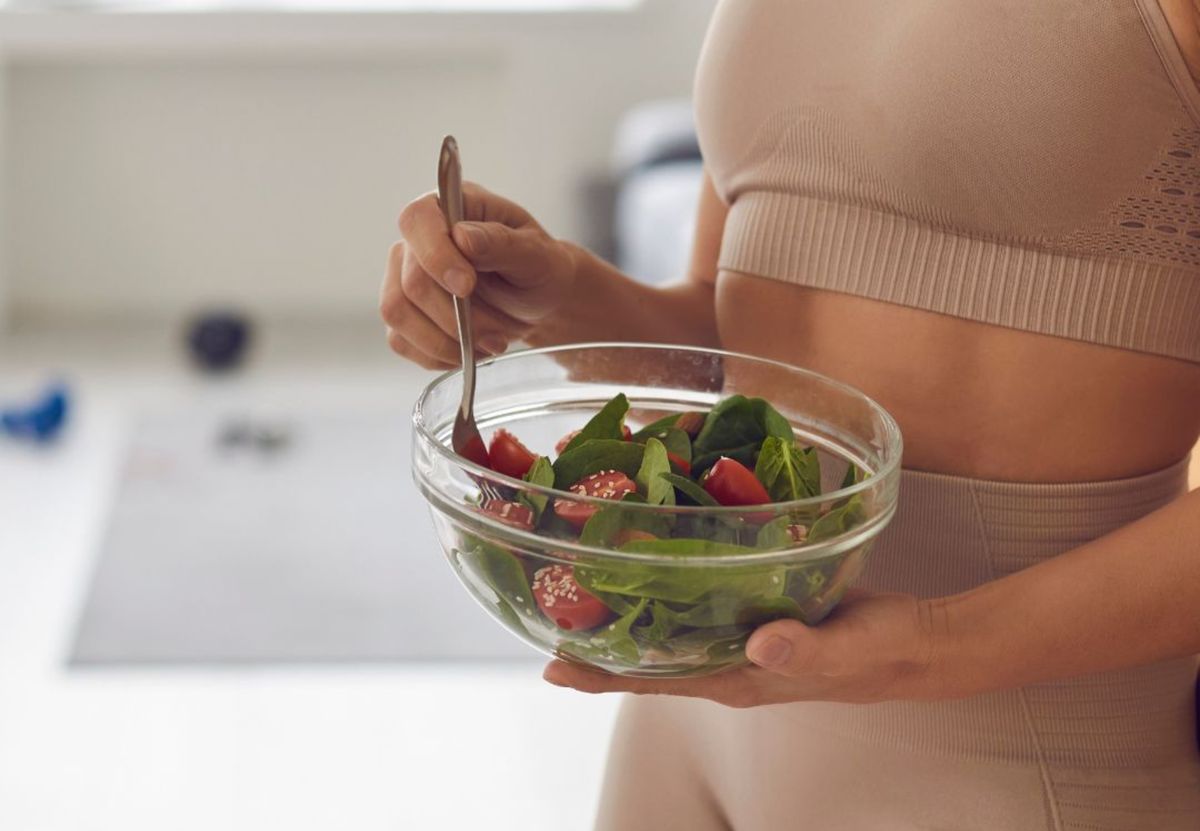 Mujer en ropa deportiva sostiene un bol de ensalada de espinacas y tomates con cuchara