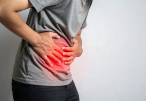 Persona con camiseta gris sujetándose el costado del abdomen con zona de dolor resaltada en rojo
